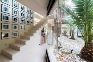 A modern staircase with a glass railing, leading to a room with a view of a palm tree and a gravel path.