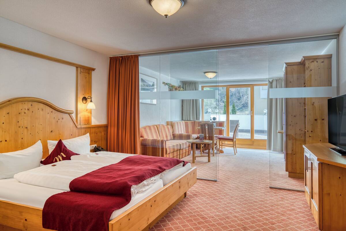 A hotel room with a wooden bed, a television, a desk, and a balcony with a view.