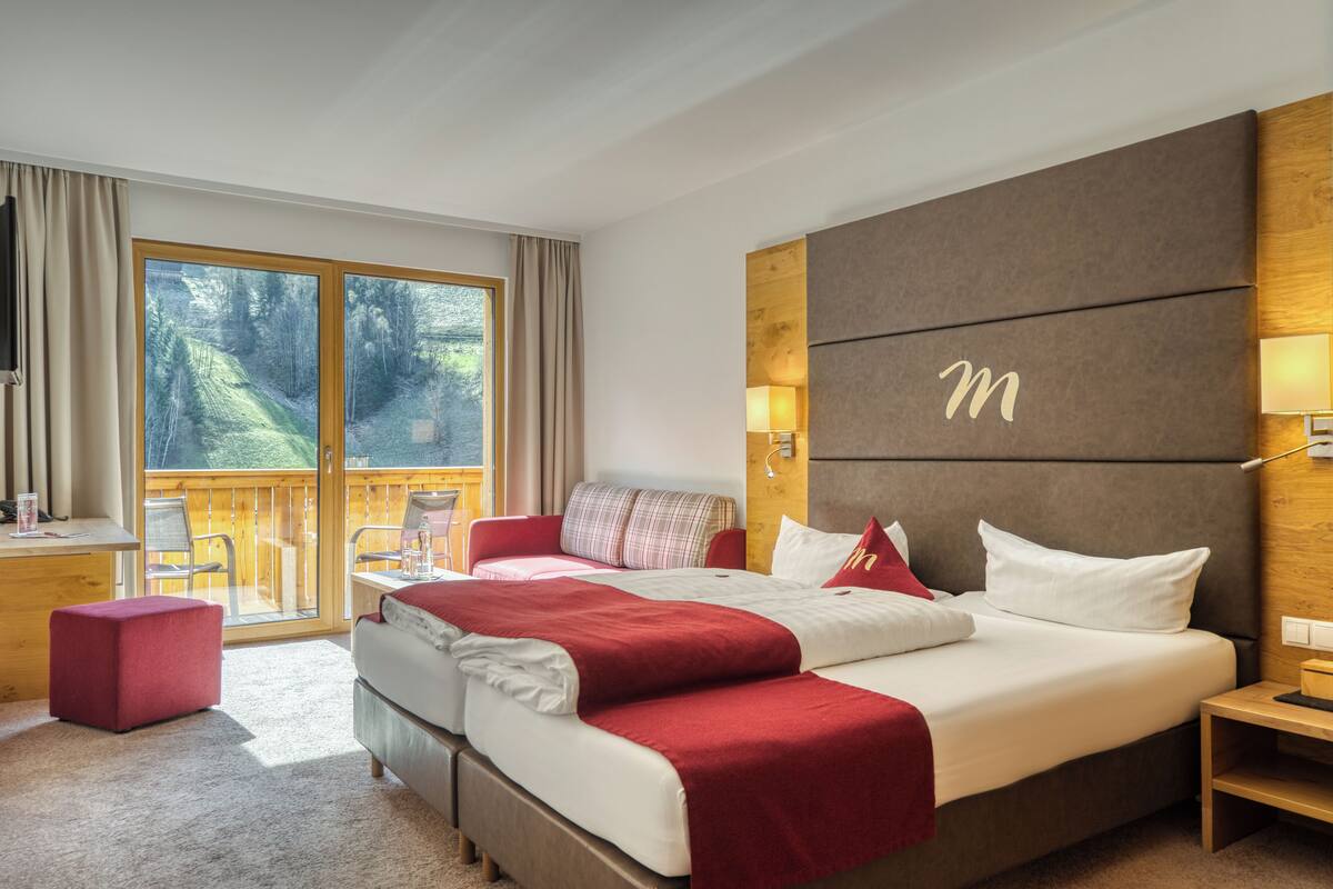 A hotel room with a large bed, a desk, and a balcony with a view of trees.