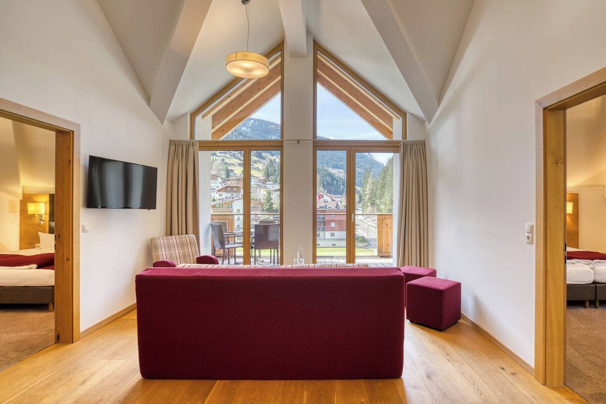 A spacious room with a large window, a flat-screen TV mounted on the wall, and a red sofa.