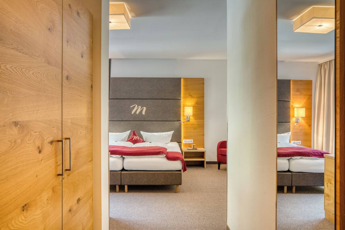 A modern hotel room with a large bed, a bedside table, a nightstand, and a wooden wardrobe.