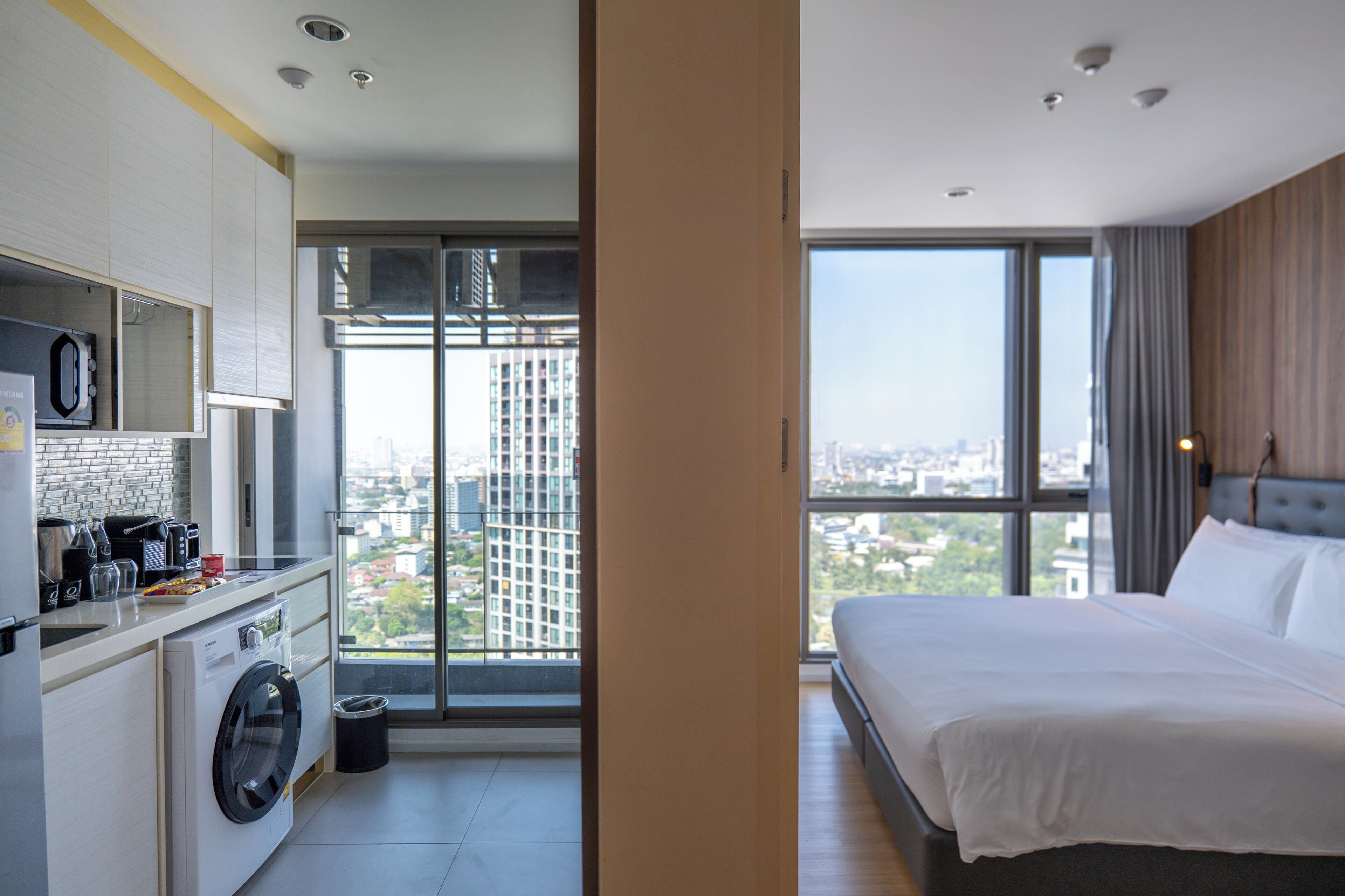Habitación de hotel con cama, lavadora, cafetera y vistas a la ciudad.