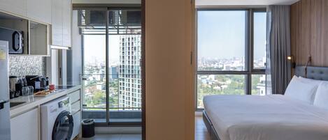 Habitación de hotel con cama, lavadora, cafetera y vistas a la ciudad.