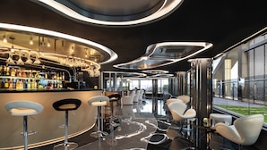Una zona de bar moderna con una barra curva, varios taburetes y un suelo negro reflectante.