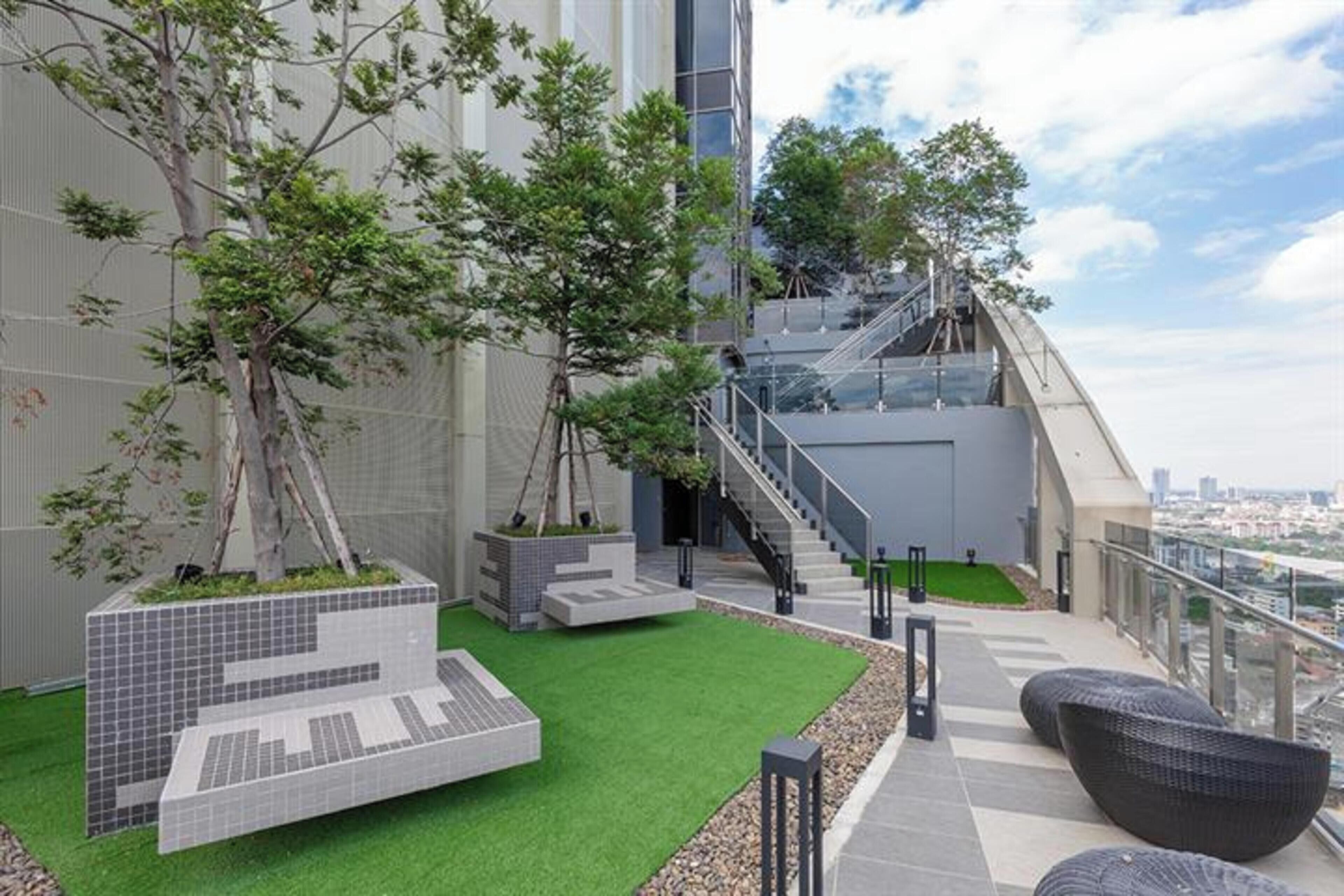 A rooftop garden with artificial grass, seating areas, and a staircase leading to an upper level.