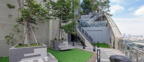 A rooftop garden with artificial grass, seating areas, and a staircase leading to an upper level.