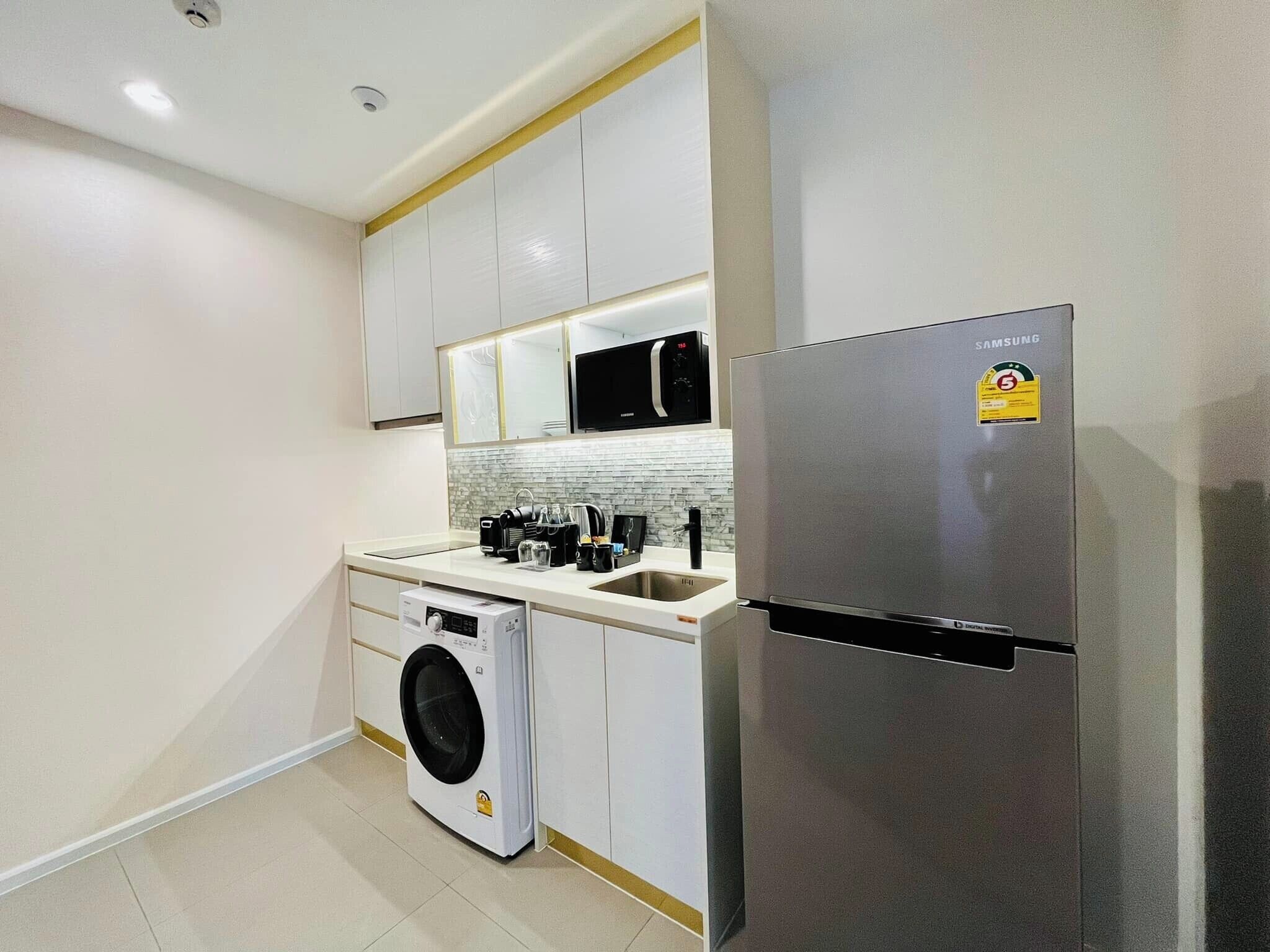 Cocina compacta con armarios blancos, un refrigerador de acero inoxidable, lavadora integrada y un microondas.