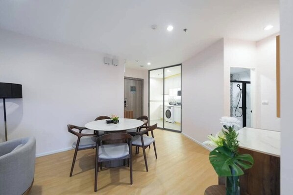 A modern dining area with a round table and chairs, a small plant, and a view into the kitchen through a glass door.