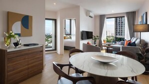Una habitación de hotel moderna con zona de comedor, sofá, televisor y vistas a la ciudad.