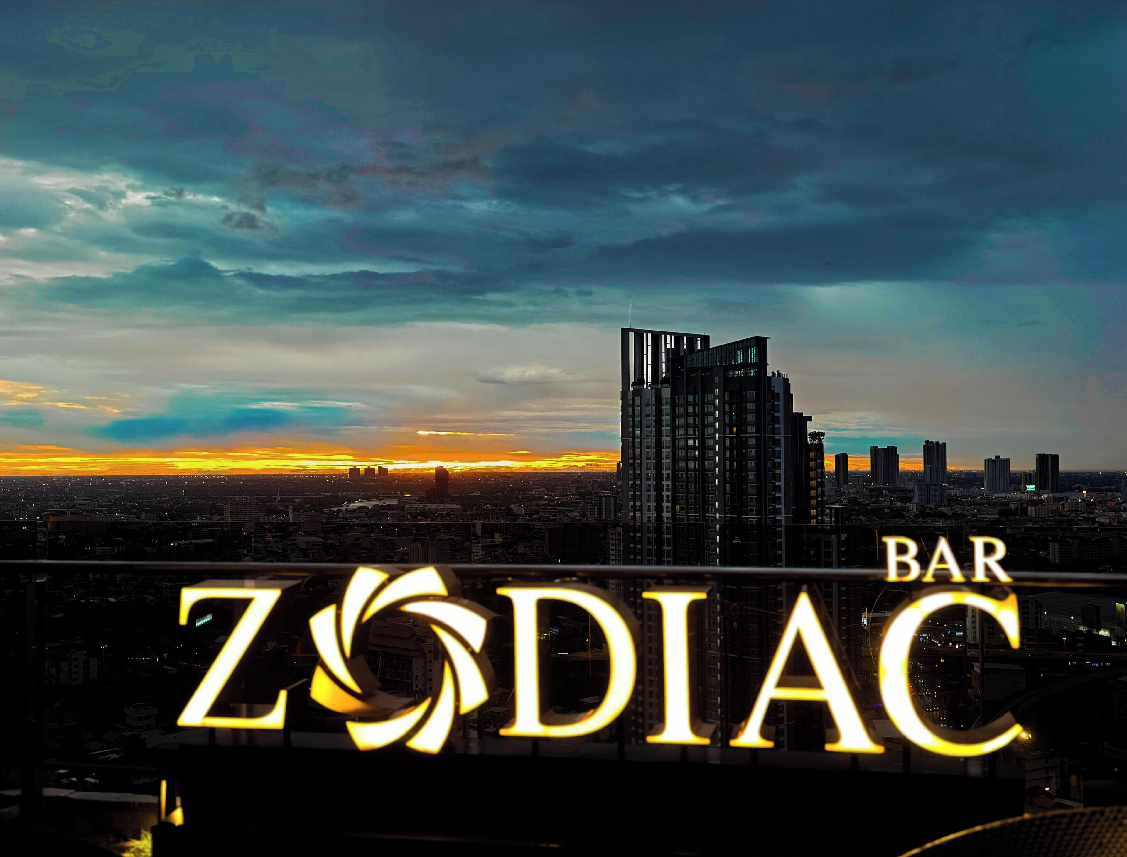 En bysilhuet i skumringen med en markant bygning i forgrunden, hvor teksten 'Zodiac Bar' lyser op.