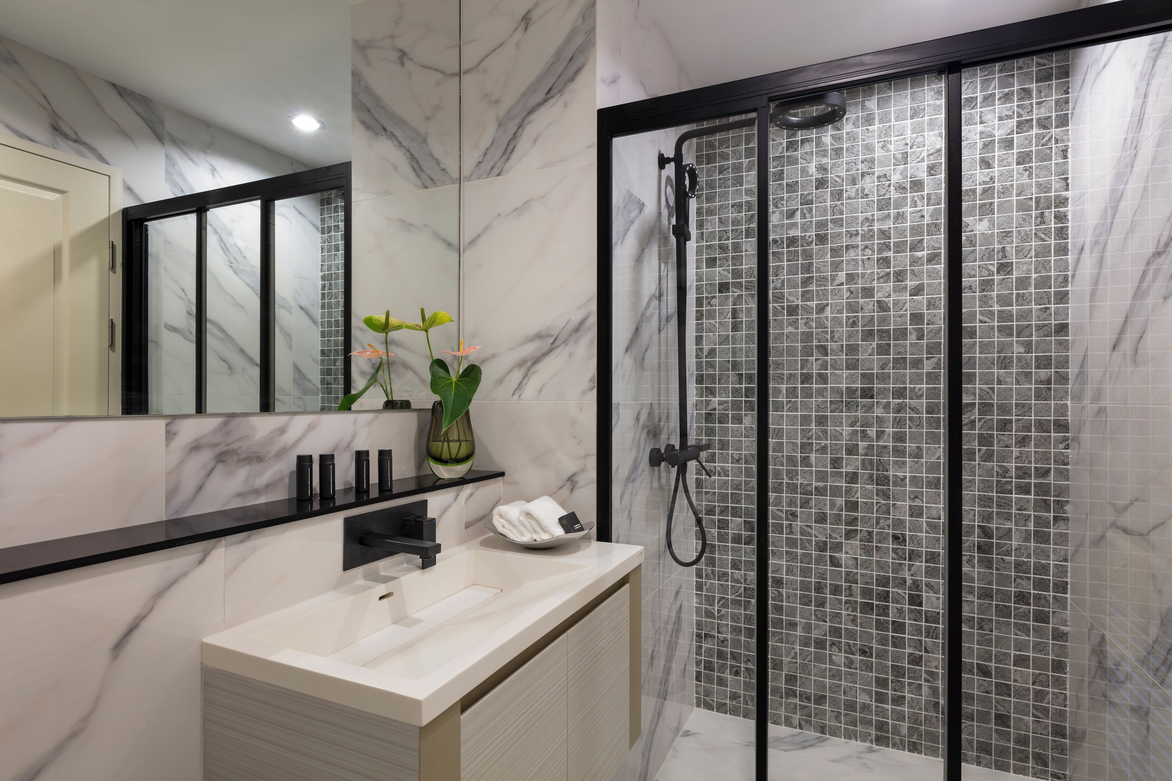 A modern bathroom with a marble vanity, a glass shower enclosure, and a large mirror.