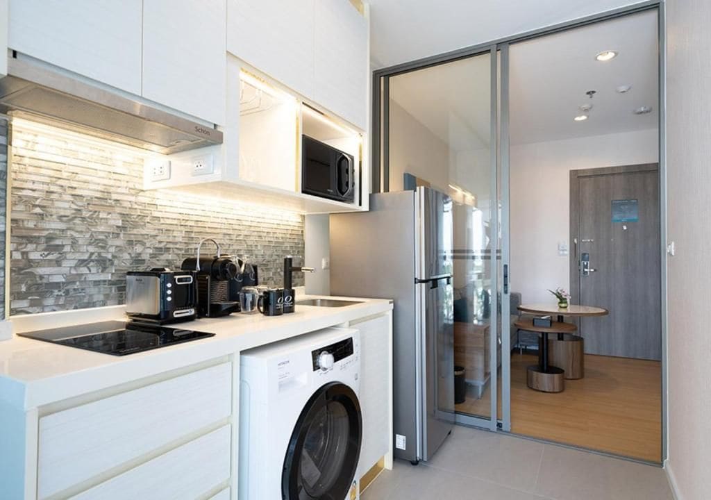 Una cocina moderna con lavadora integrada, microondas y refrigerador de acero inoxidable.