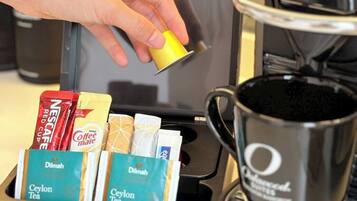 A coffee machine with a hand holding a coffee pod, a coffee pot, and a tray with various coffee pods and a tea bag.