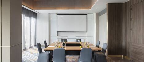 Une salle de conférence équipée d’une grande table, de chaises, d’un écran de projection et d’un sol recouvert de moquette.