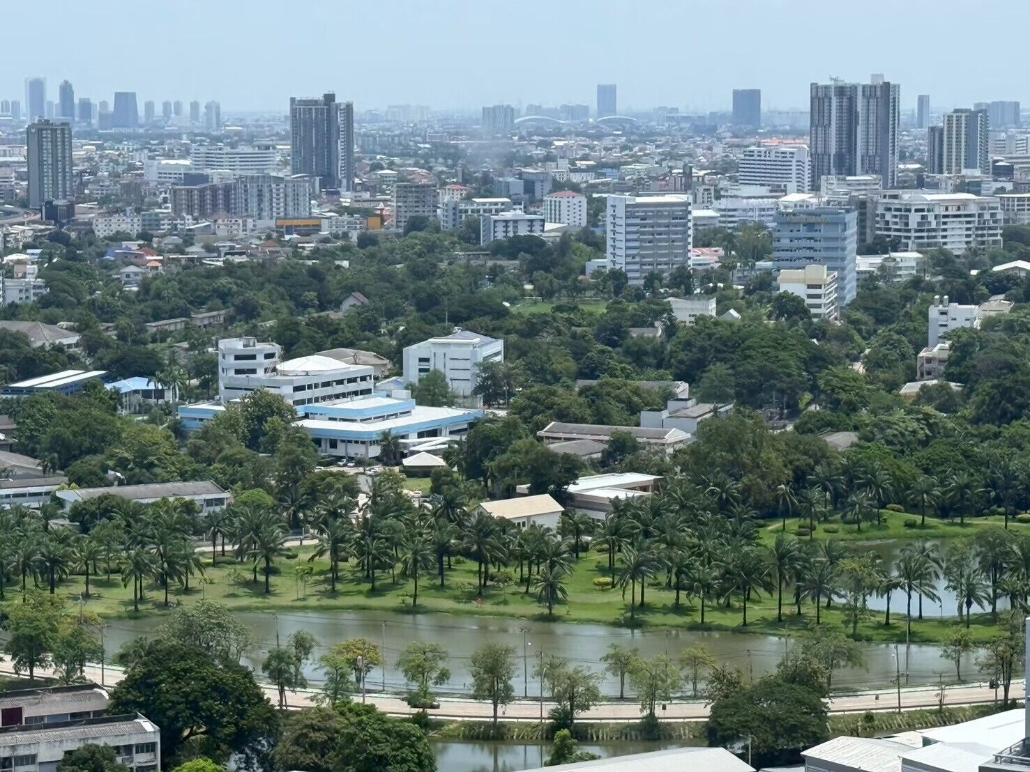 A cityscape with a mix of high-rise buildings and low-rise structures, surrounded by greenery and a body of water.