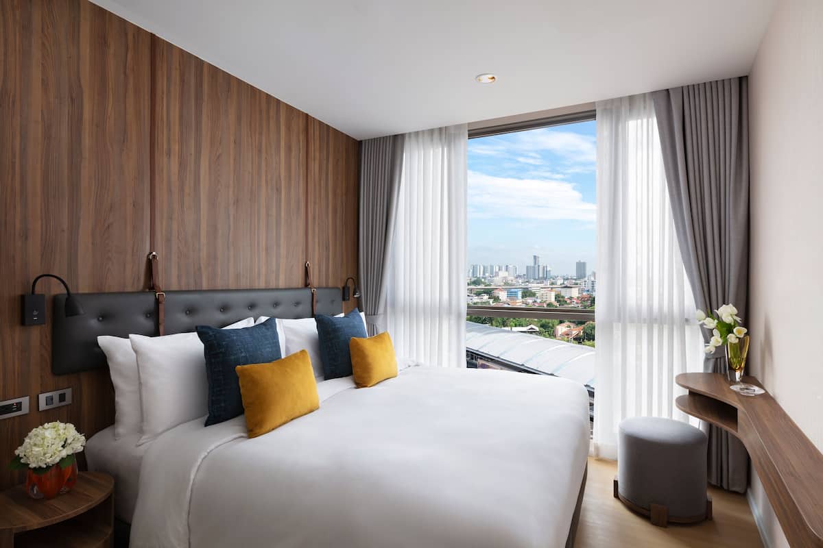 Een moderne hotelkamer met een groot bed, uitzicht over de stad en een houten accentmuur.