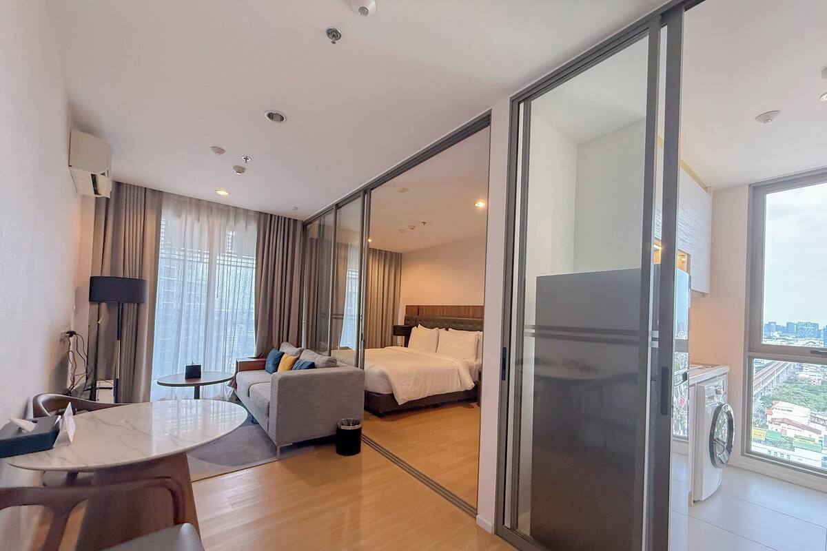 Een moderne hotelkamer met een bed, een bureau, een stoel, een bijzettafeltje en een groot raam met uitzicht op de stad.