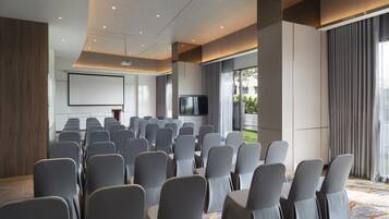 Ein Konferenzraum mit Reihen von Stühlen, einer Projektionsleinwand und einem Fernseher.
