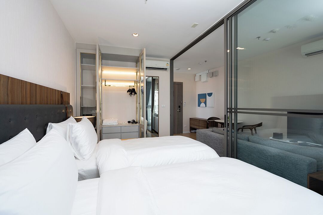 Une chambre d’hôtel moderne dotée d’un grand lit, d’un coin salon avec un canapé et des fauteuils, et d’une cloison en verre qui sépare la chambre d’un espace repas.