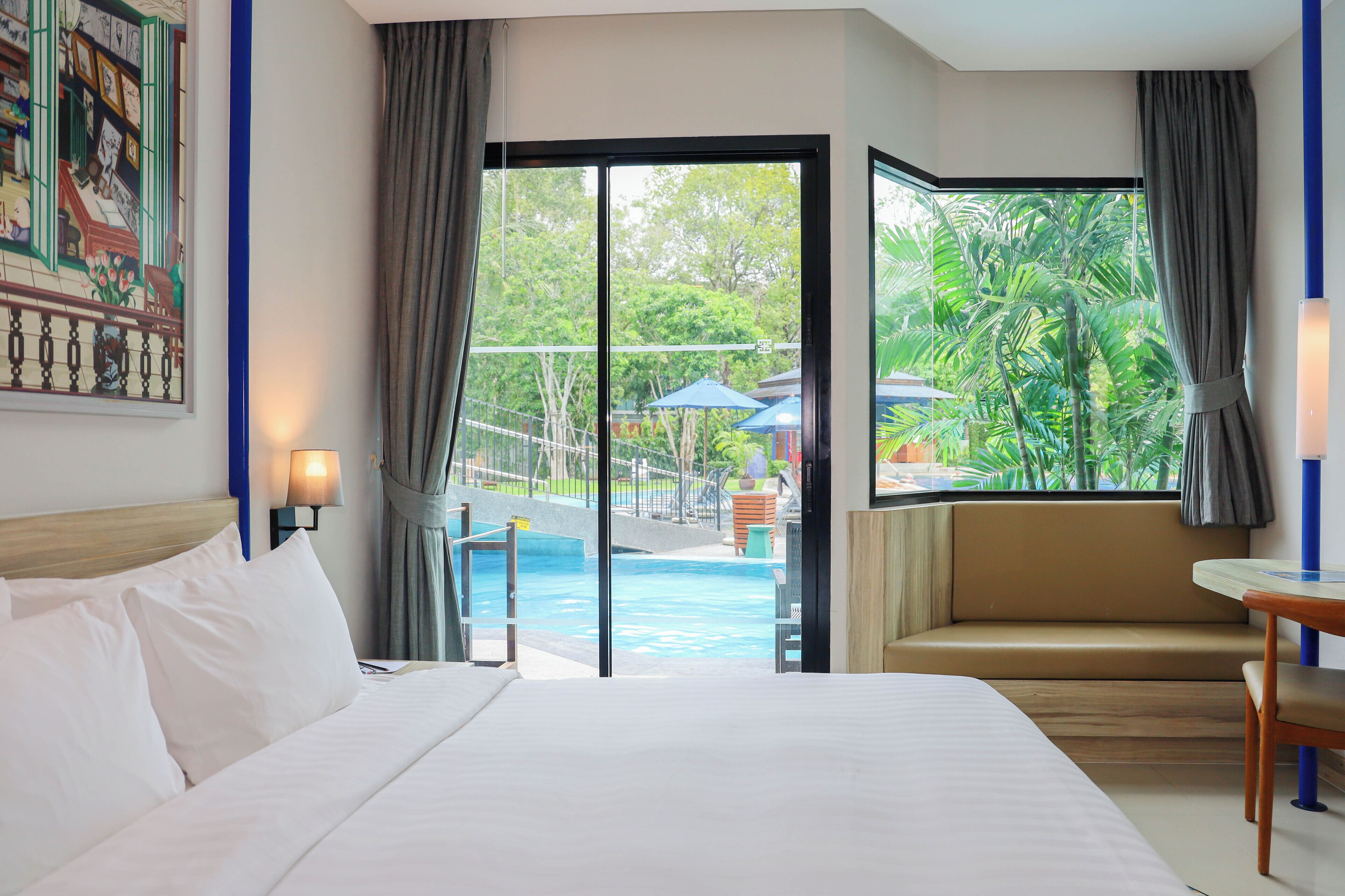 Habitación de hotel con cama, sofá, mesa y vistas a una piscina y zonas verdes.