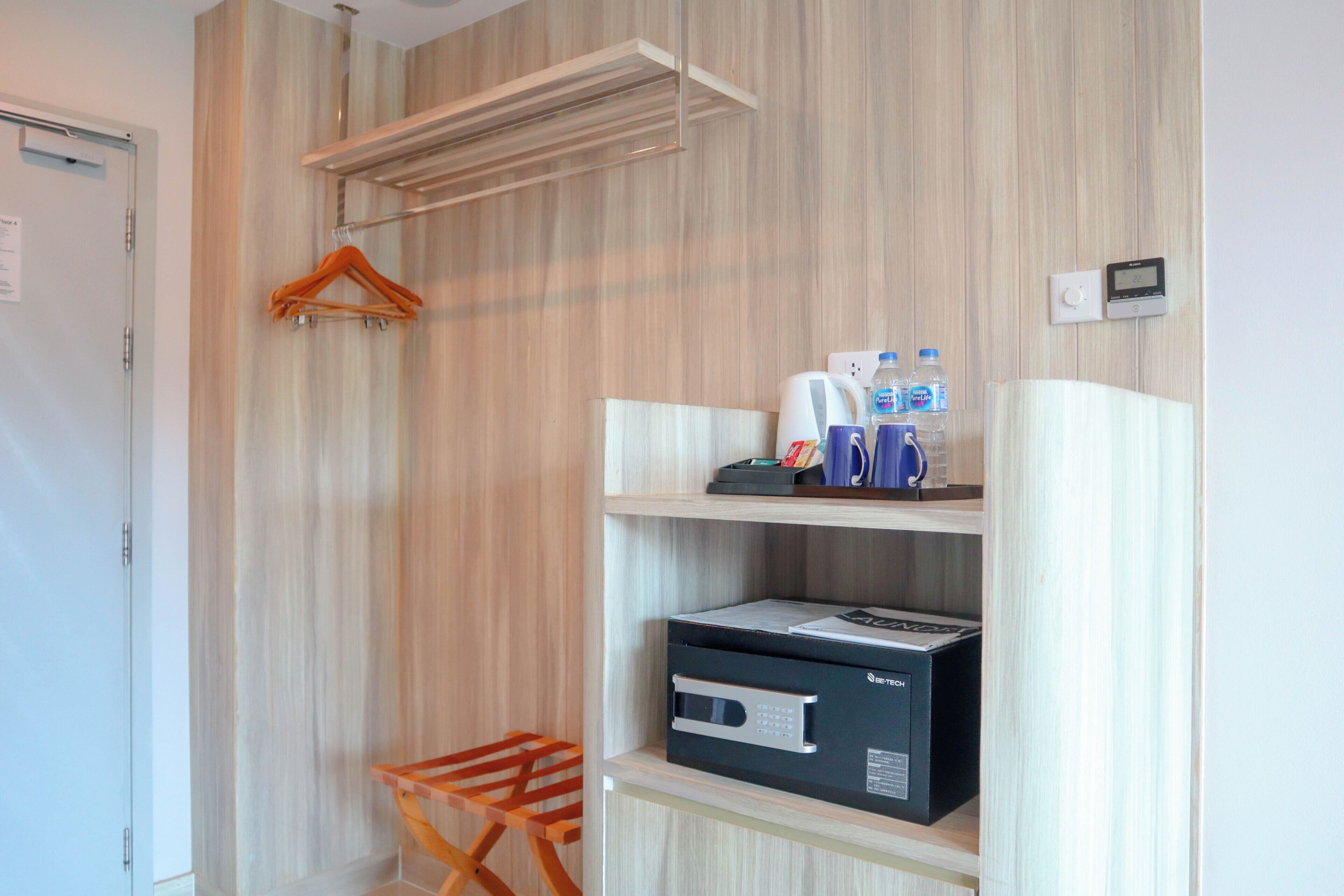 Habitación de hotel con pared de madera, perchero, estante con artículos de aseo, microondas y un pequeño cubo de basura.