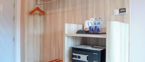 Habitación de hotel con pared de madera, perchero, estante con artículos de aseo, microondas y un pequeño cubo de basura.