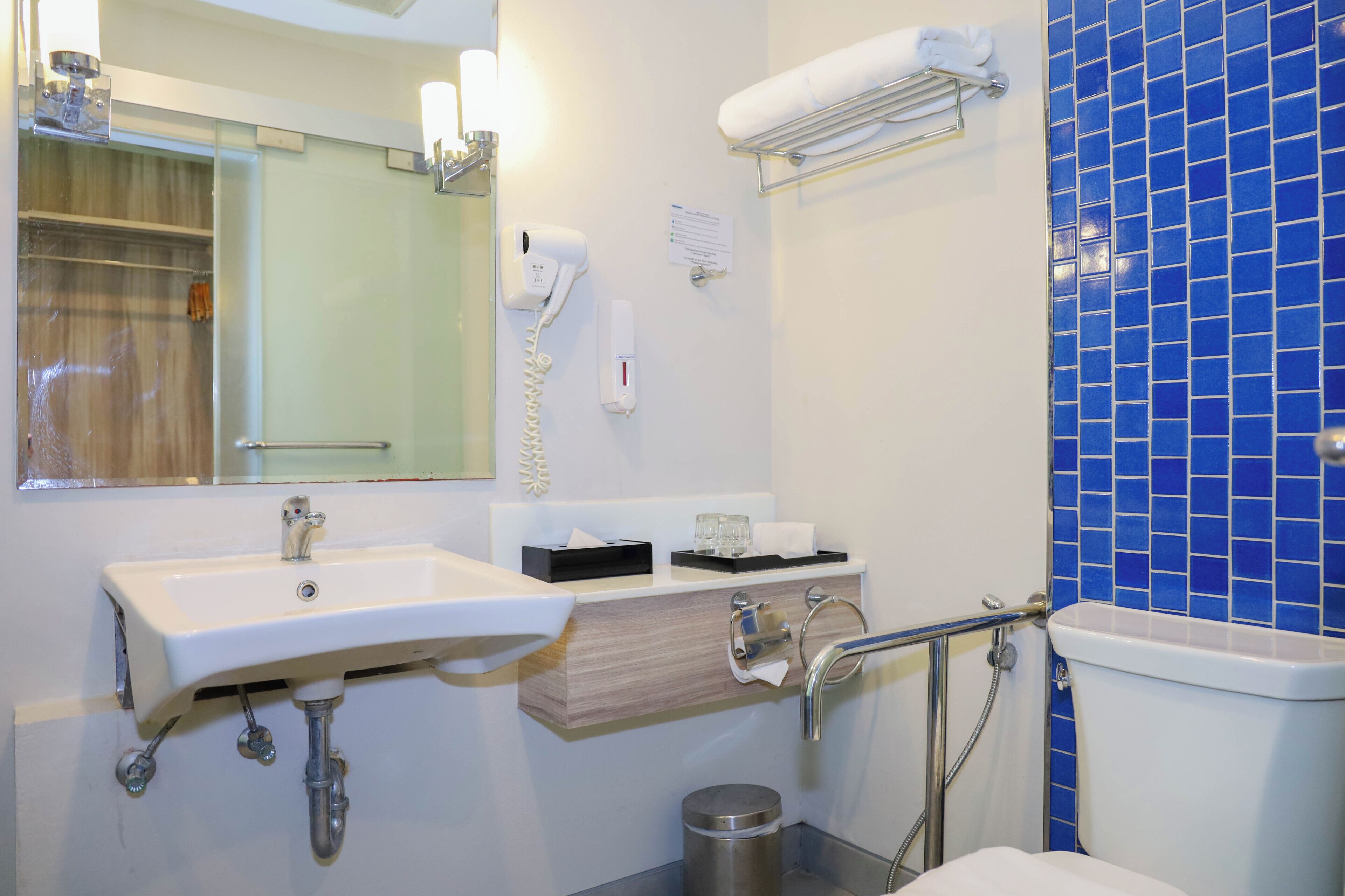 A bathroom with a sink, mirror, towel rack, and blue-tiled wall.