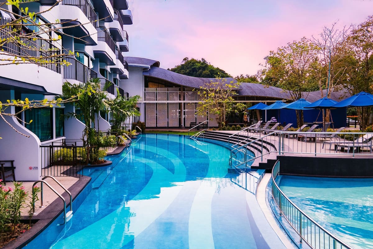 A swimming pool surrounded by modern buildings, with lounge chairs and umbrellas.