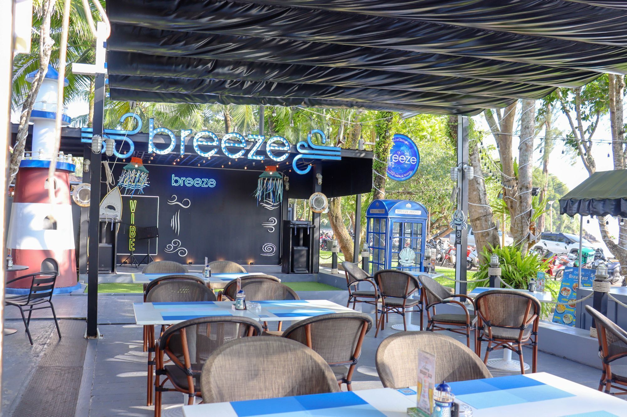 An outdoor seating area with tables and chairs, a neon sign reading "breeze," and a blue telephone booth.