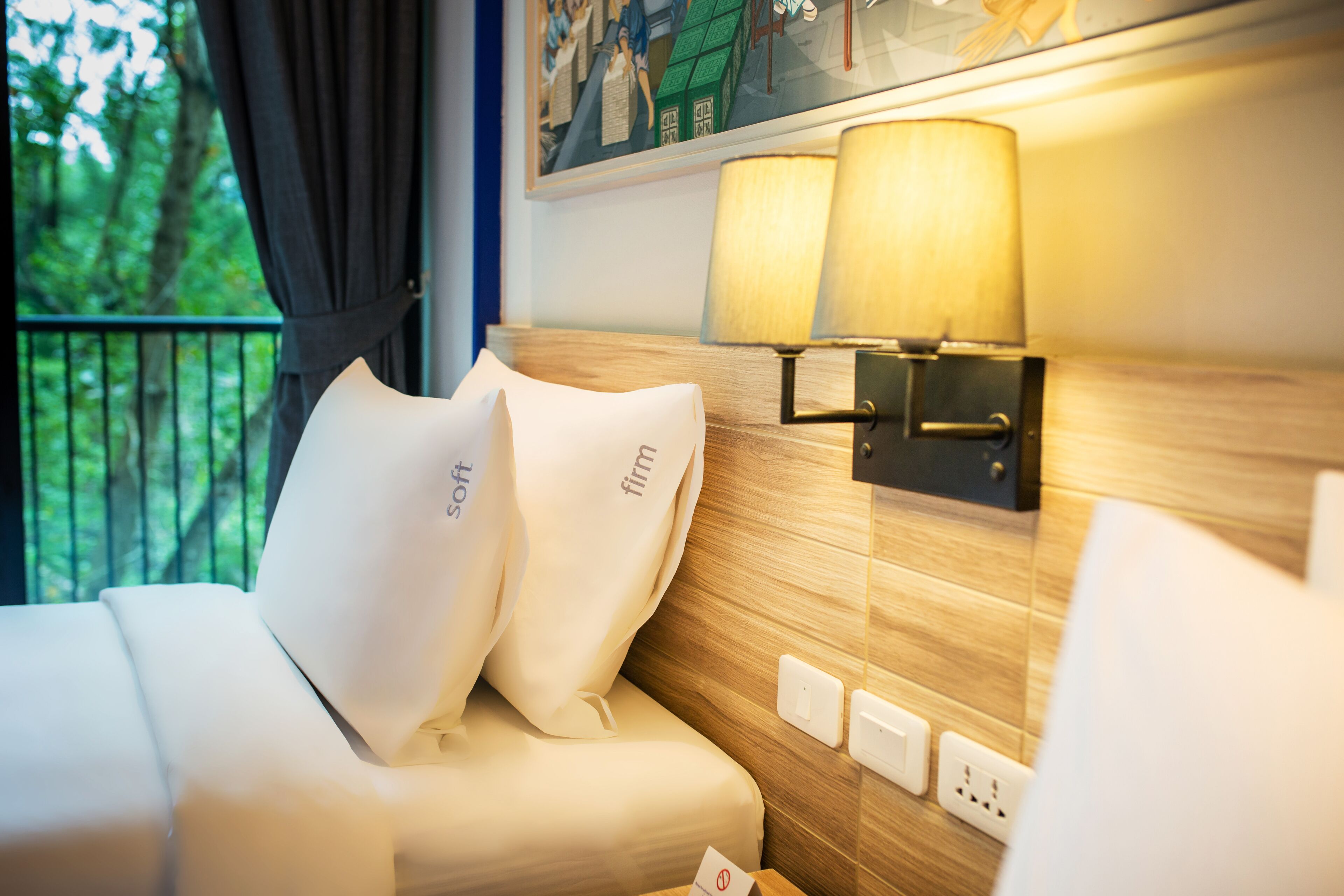 A hotel room with a bed, two pillows, a nightstand, a lamp, and a painting on the wall.