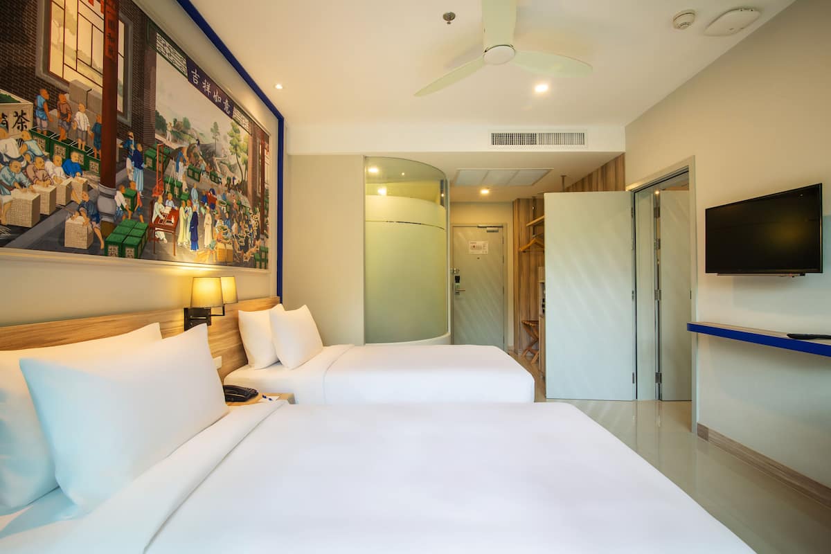A hotel room with two beds, a ceiling fan, a television, and a mural on the wall.