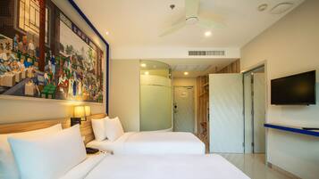A hotel room with two beds, a ceiling fan, a television, and a mural on the wall.