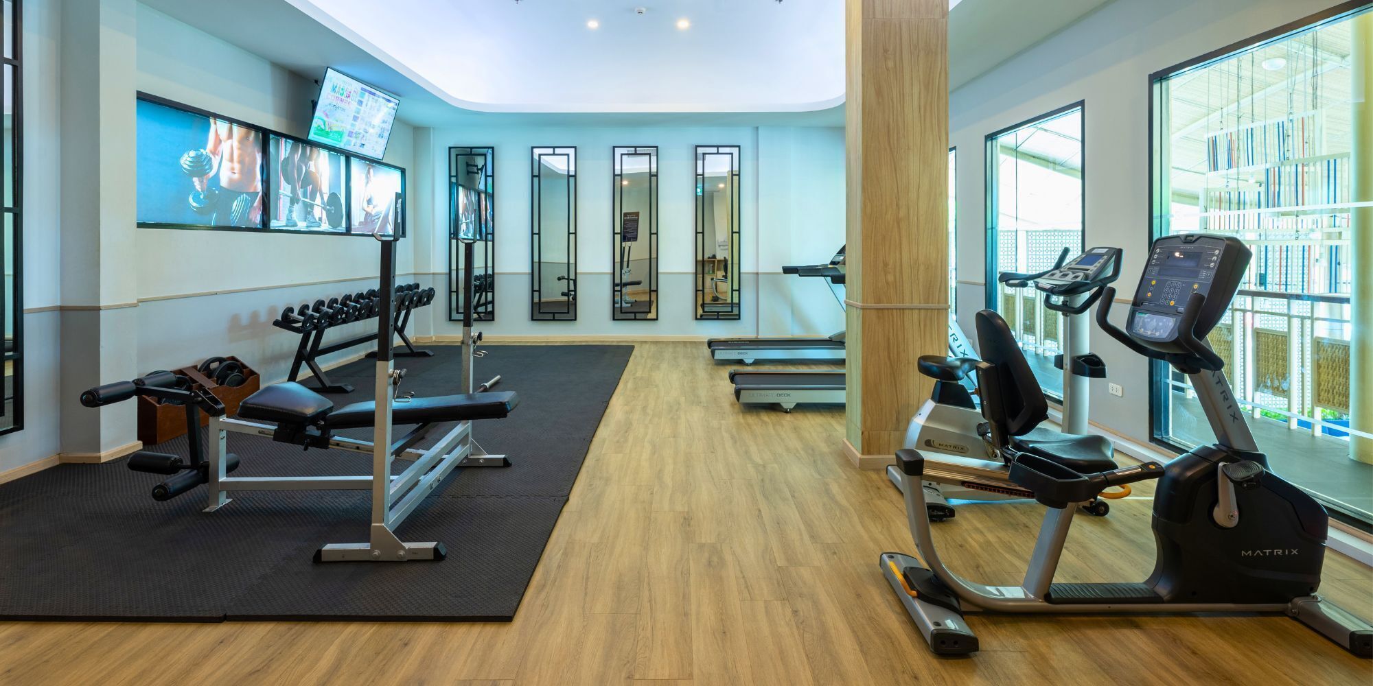 Ett gym med konditionsmaskiner, styrketräningsmaskiner och en tv-skärm som visar träningsvideor.