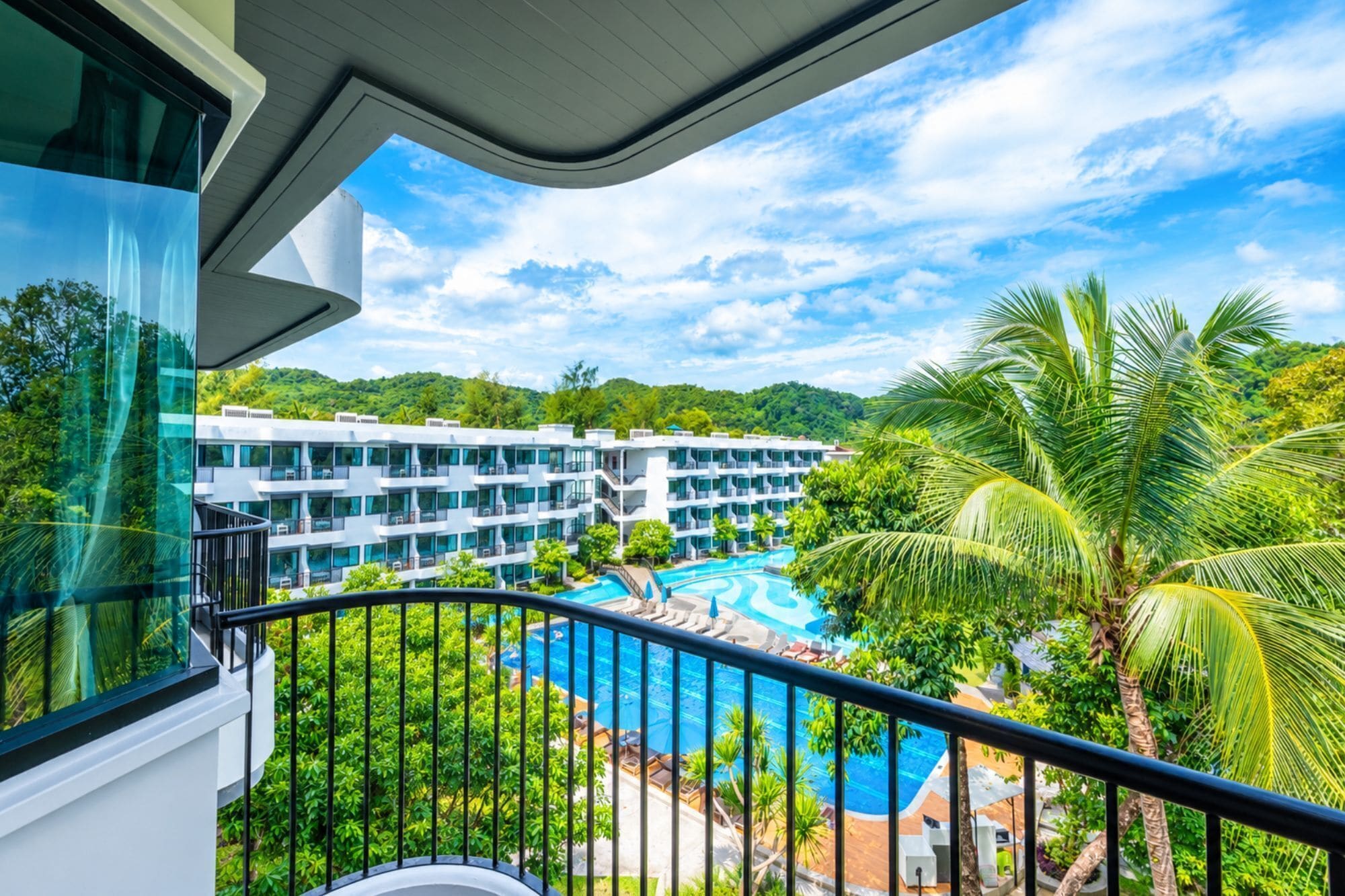 A hotel with a pool, surrounded by lush greenery and palm trees.