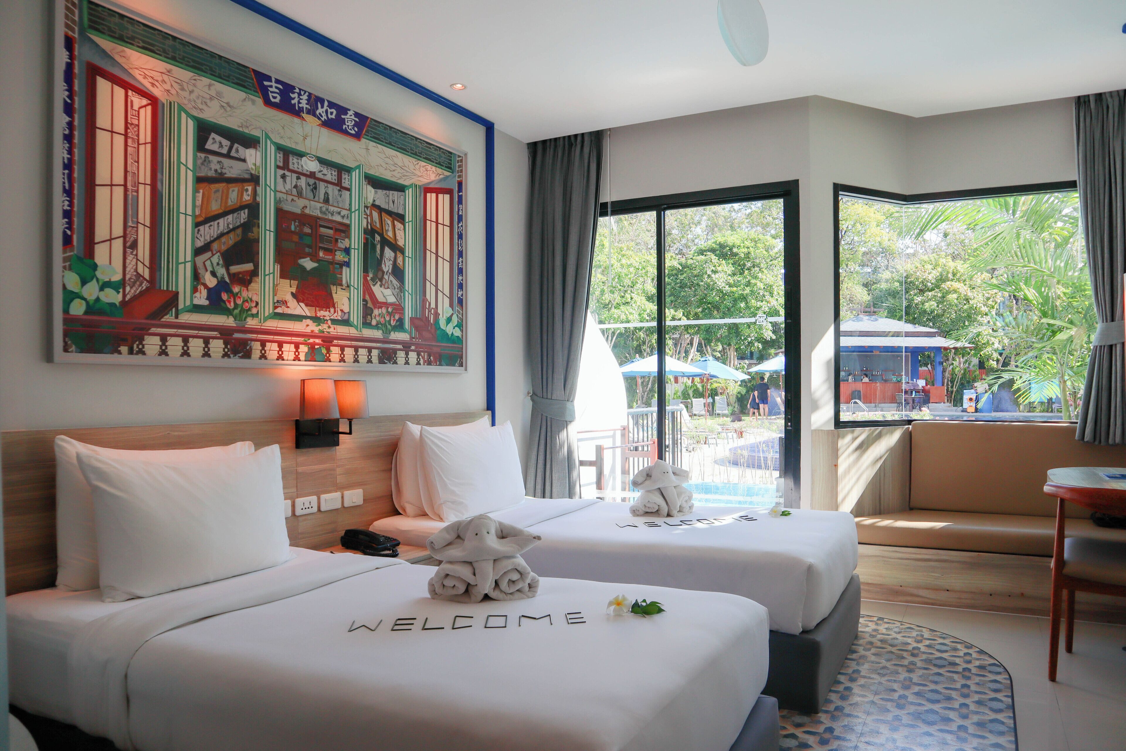 A hotel room with two beds, a large window with a view of a pool and palm trees, and a painting on the wall.
