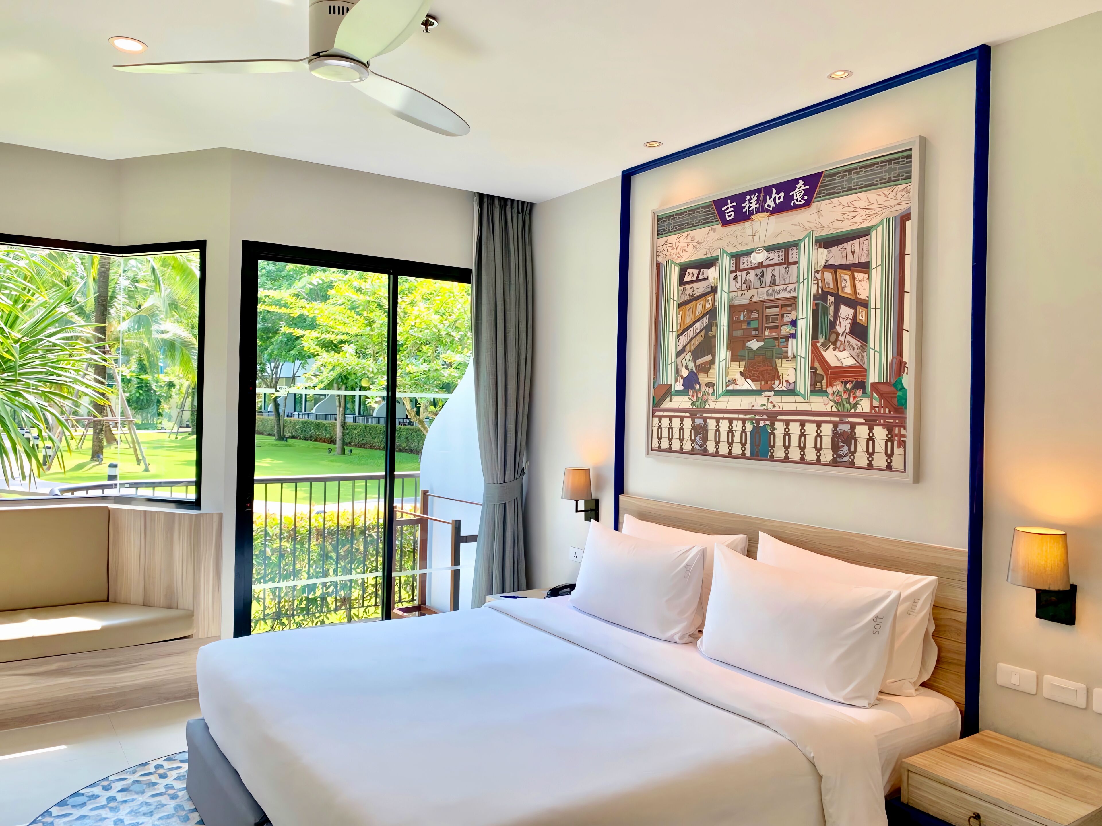A hotel room with a large bed, a balcony with a view of greenery, and a wall-mounted artwork.