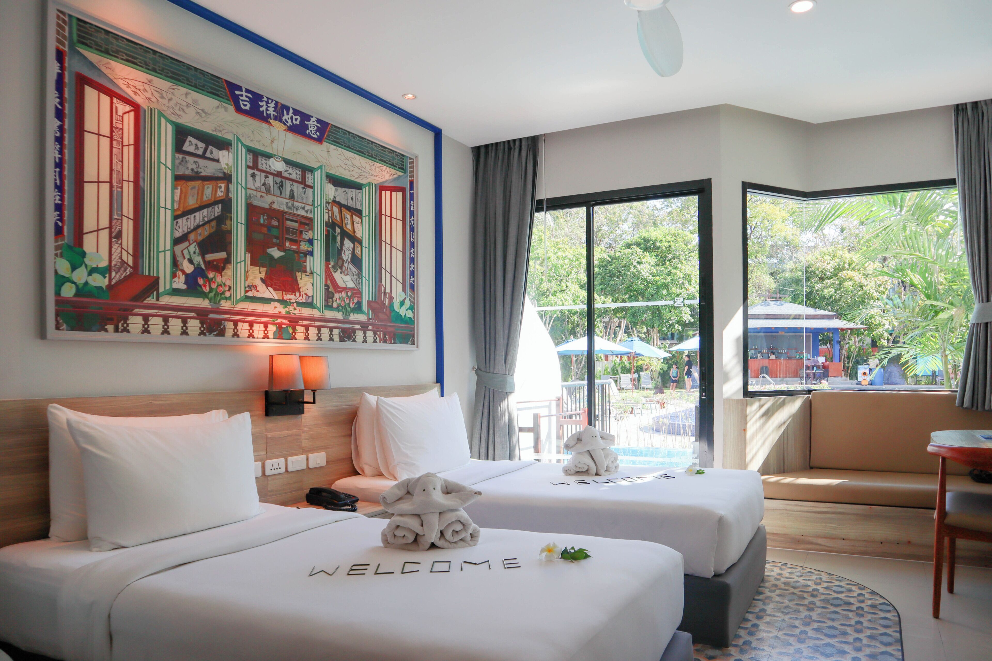 A hotel room with two beds, a large mural, a view of the outdoors, and a pool area visible through the window.