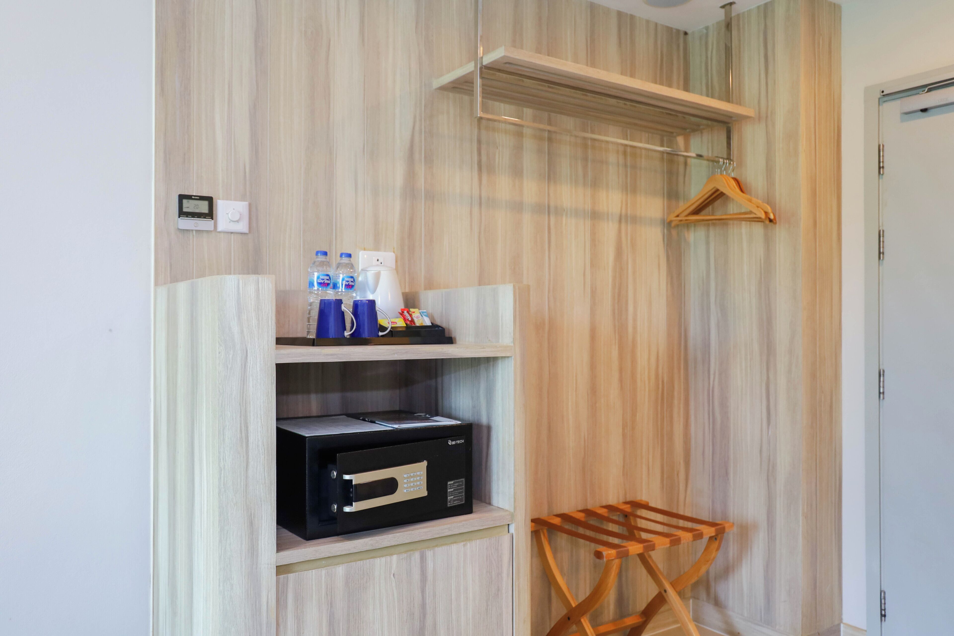 A room with a wooden panel wall, a black appliance on the lower shelf, a wooden hanger on the wall, and a small wooden folding chair.