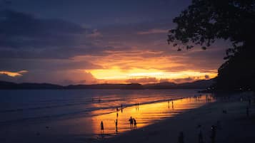 Una playa al atardecer con gente caminando por la orilla.