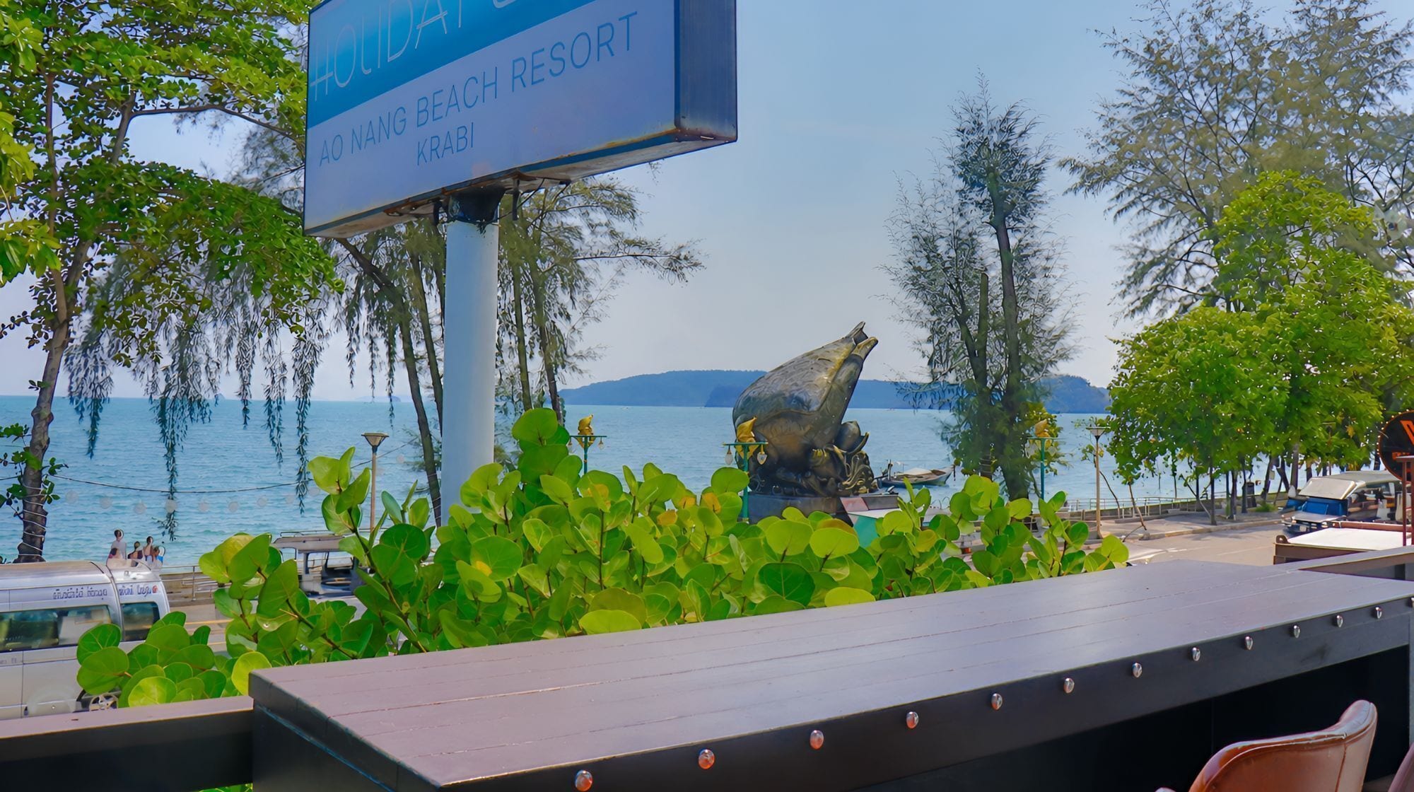 A sign for Ao Nang Beach Resort, a view of the sea, and a statue.