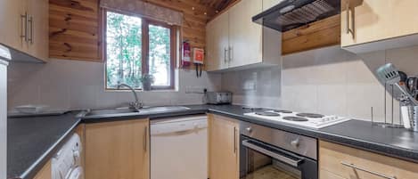 Une cuisine moderne avec des meubles en bois, un lave-vaisselle, un four, une cuisinière et une fenêtre donnant sur des arbres.