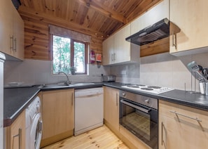 Une cuisine moderne avec des meubles en bois, un lave-vaisselle, un four, une cuisinière et une fenêtre donnant sur des arbres.