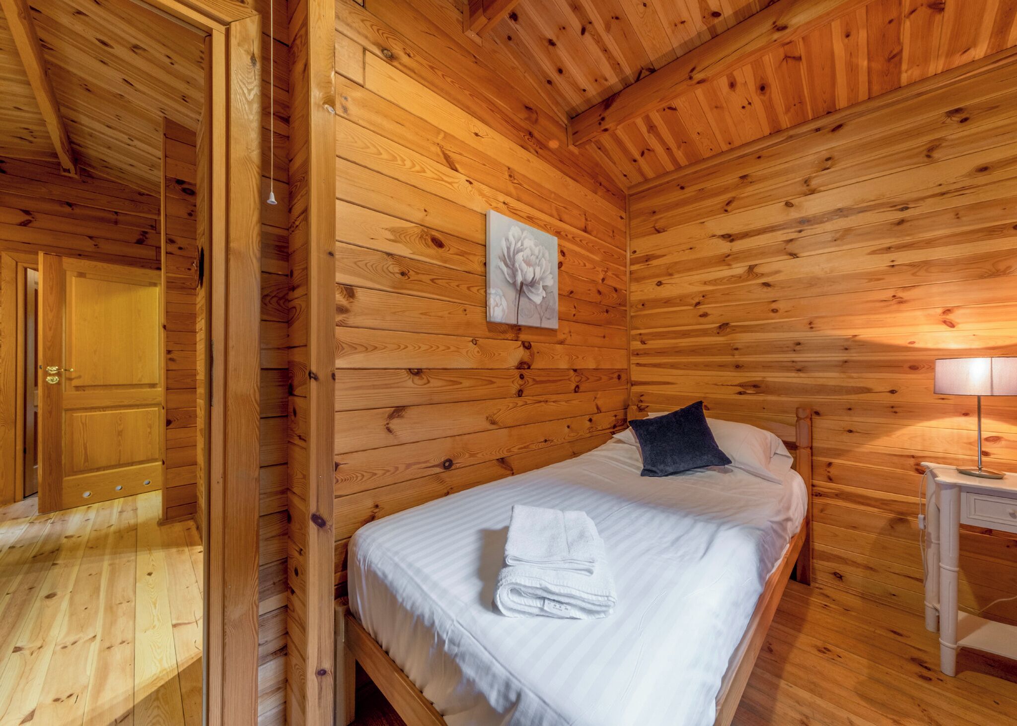Une pièce de cabane en bois comprenant un lit, une table de chevet, une lampe et une porte.