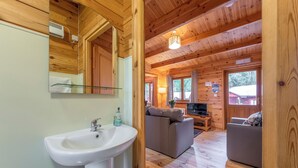 A wooden cabin interior with a bathroom, a sofa, a TV, and a dining area.