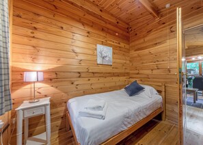 A wooden-paneled room with a bed, a nightstand, a lamp, and a door leading outside.