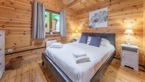 A wooden-paneled bedroom with a bed, two bedside tables with lamps, a window with curtains, and a wall-mounted orchid painting.