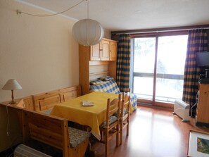 Cozy dining area with a table for two, bench, and single chair, plus a mounted TV and large window.