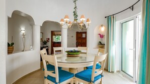 A dining area with a round glass table, six chairs with blue cushions, a chandelier, and a view of the outdoors through a sliding glass door. - Casa Sonny - villa with airco and pool near golf course, beaches and town (Carvoeiro)