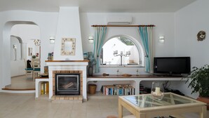 A living room with a fireplace, a television, and a bookshelf. - Casa Sonny - villa with airco and pool near golf course, beaches and town (Carvoeiro)