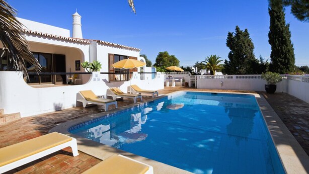 A swimming pool with lounge chairs and umbrellas, surrounded by a white building with a tiled roof. - Casa ADM 42 - Villa with Pool, Walk to Carvoeiro (Lagoa)